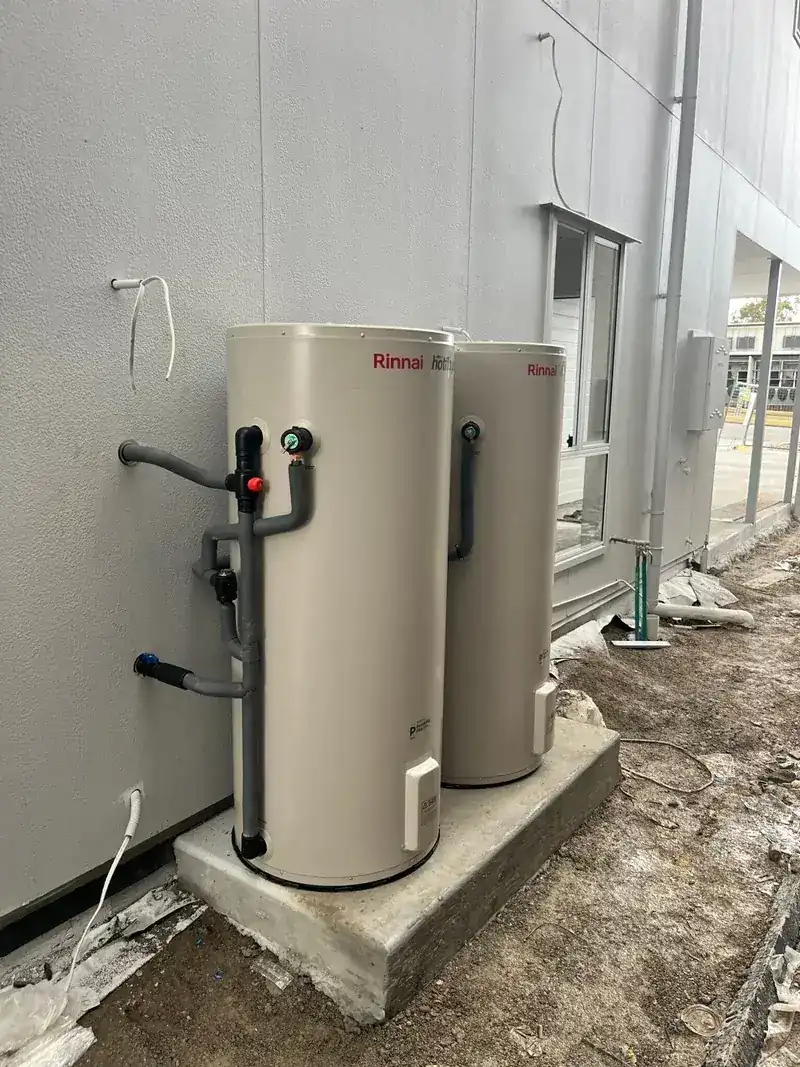 Two Rinnai electric hot water storage tanks installed side by side on a concrete pad against a building wall