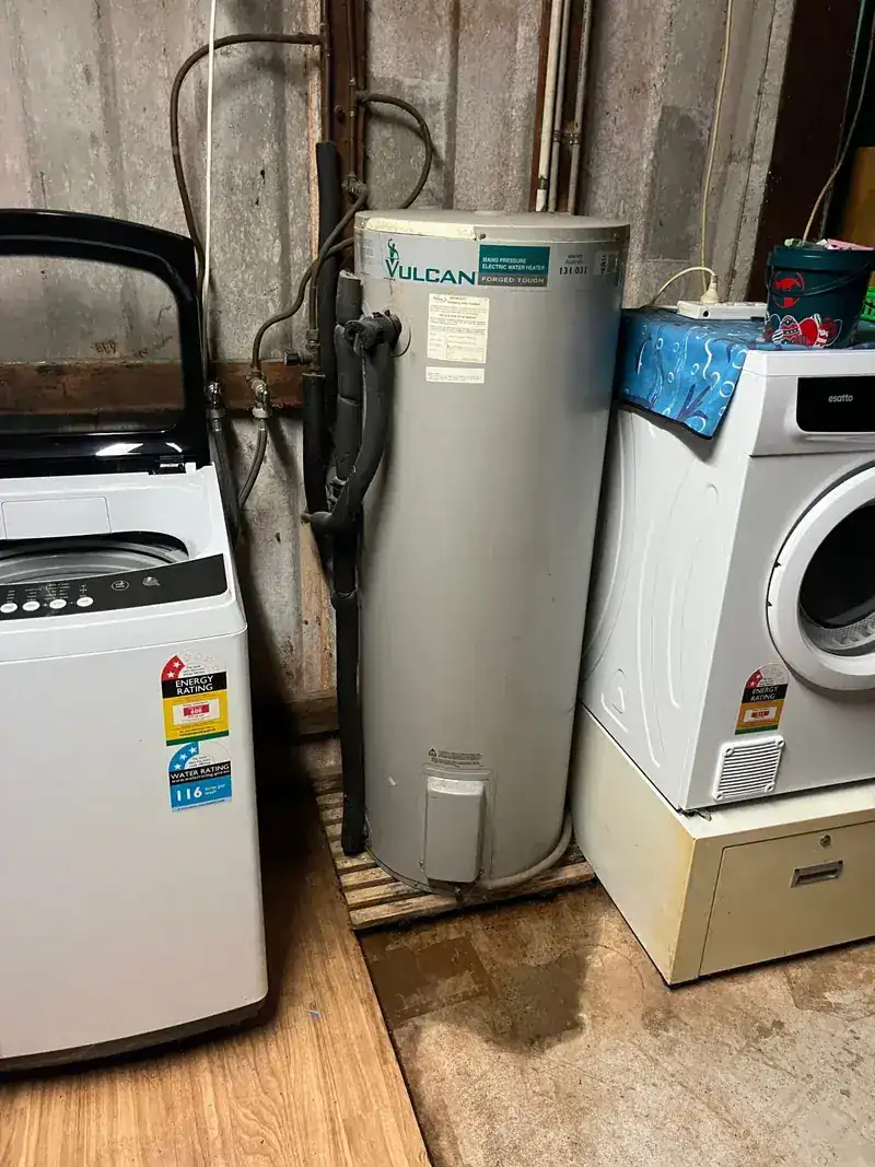 A Vulcan hot water storage tank installed in a narrow internal laundry between a washing machine and a dryer