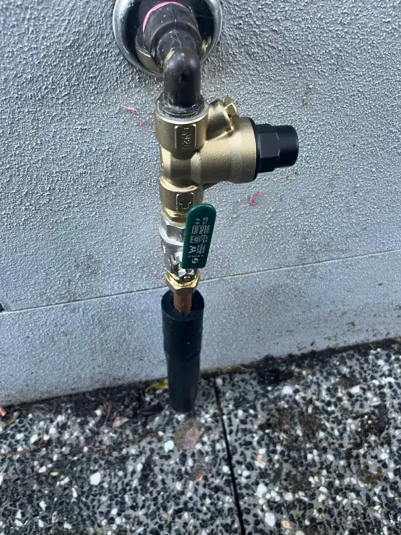 A brass tempering valve fitted to hot water pipework with a new black relief drain line